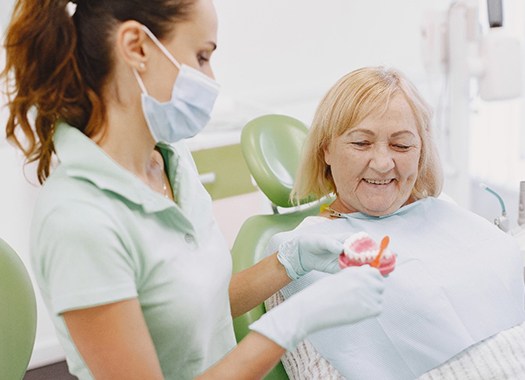 An older woman watches a dentist show her how to take care of All-On-4 dental implants 