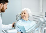 An older woman smiles as she listens to her dentist discuss alternative options to pay for dental implants