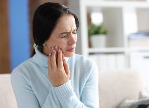 Woman struggling with tooth pain on couch at home